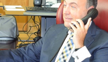 NFB President Mark Riccobono listens to NFB-NEWSLINE on the phone at his desk.